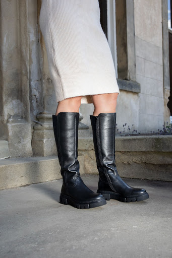 An image of a girl wearing a black pair of knee-high boots with a jumper dress