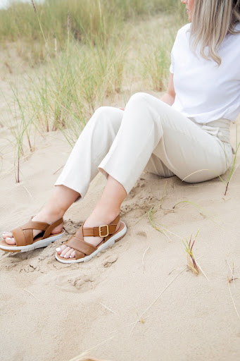 An image of a woman sitting on the beach wearing flat tan sandals