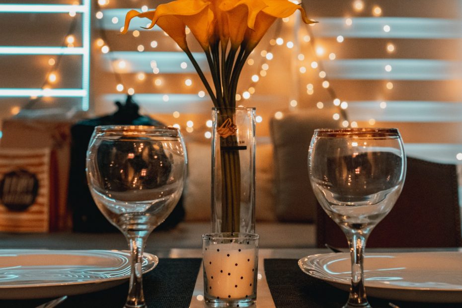 Two empty wine glasses are at the forefront of the image. There are fairy lights and orange flowers in the background.