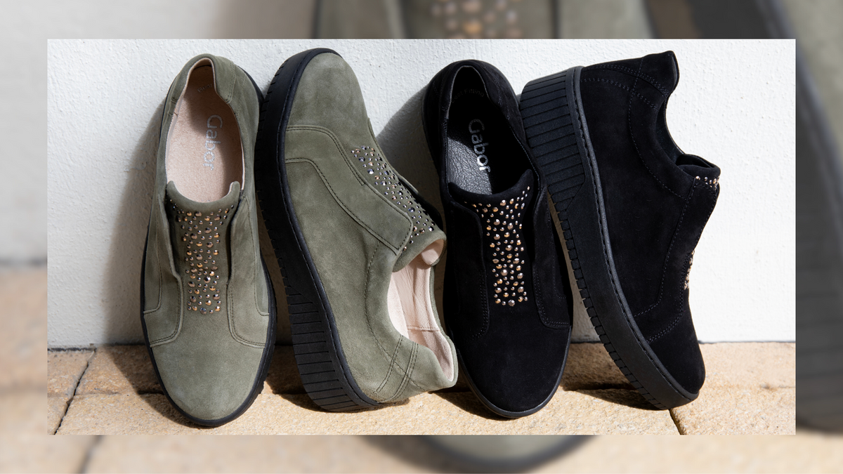 Two pairs of Gabor Wonderland shoes in olive and black suede are set against a white wall.