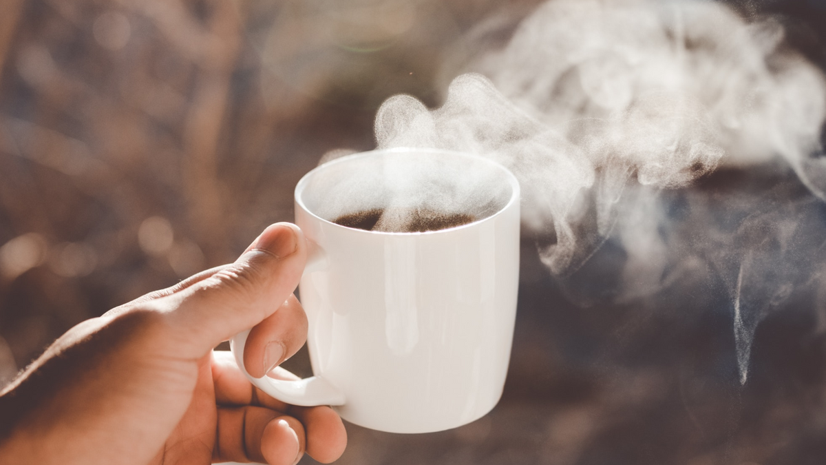 A hand holds up a cup of coffee in a white mug.