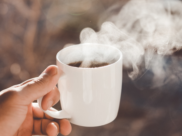 A hand holds up a cup of coffee in a white mug.