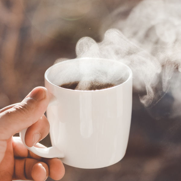 A hand holds up a cup of coffee in a white mug.