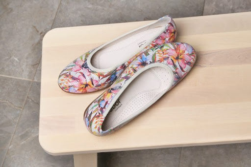 An image of a pair of pink floral ballet flats on a bench