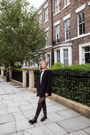 Image of a model wearing black knee high boots with tights, a grey jumper and a blazer