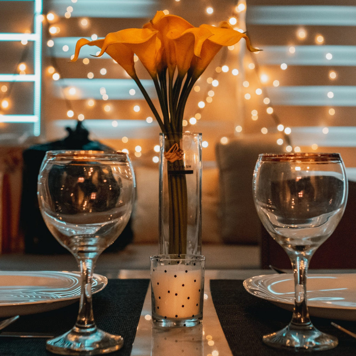 Two empty wine glasses are at the forefront of the image. There are fairy lights and orange flowers in the background.