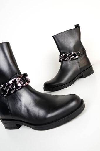 An image of a black pair of ankle boots with silver chain detail